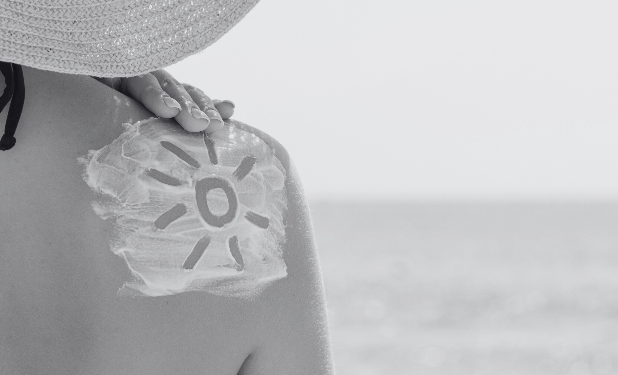 Black and white photo of a woman’s back with sunscreen applied in the shape of a sun
