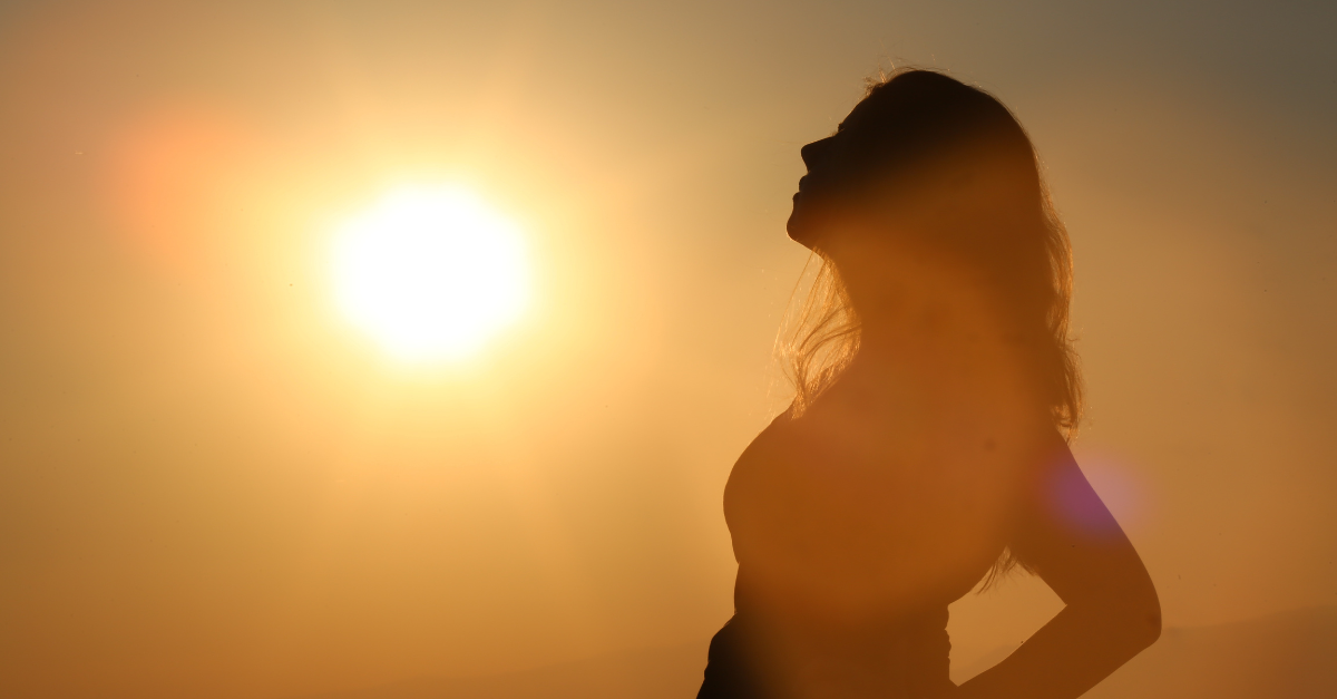 Silhouette of a woman standing under the sun, facing the light, symbolizing natural healing and connection to sunlight.